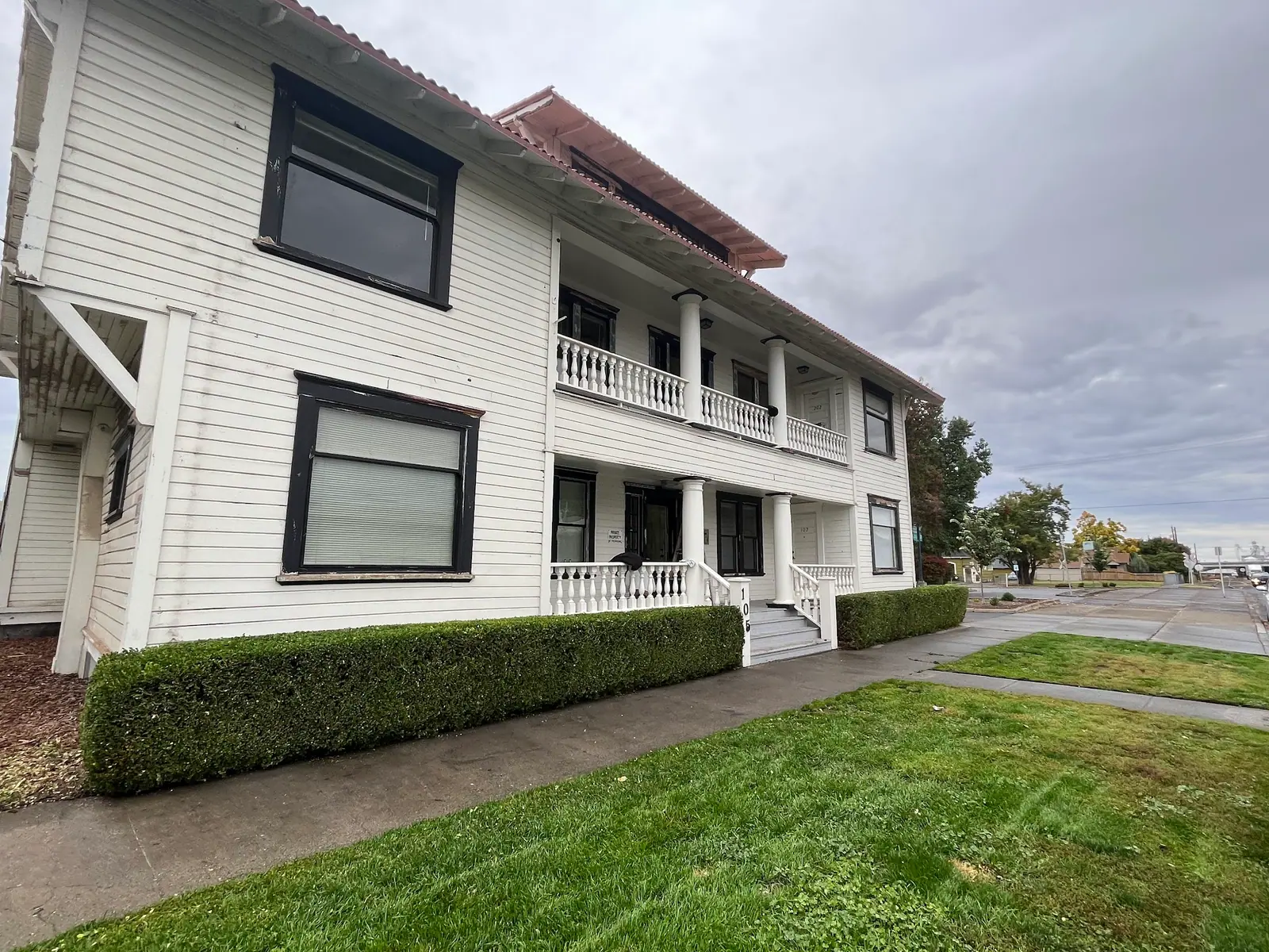 White two-storey house with a trimmed hedge and lawn